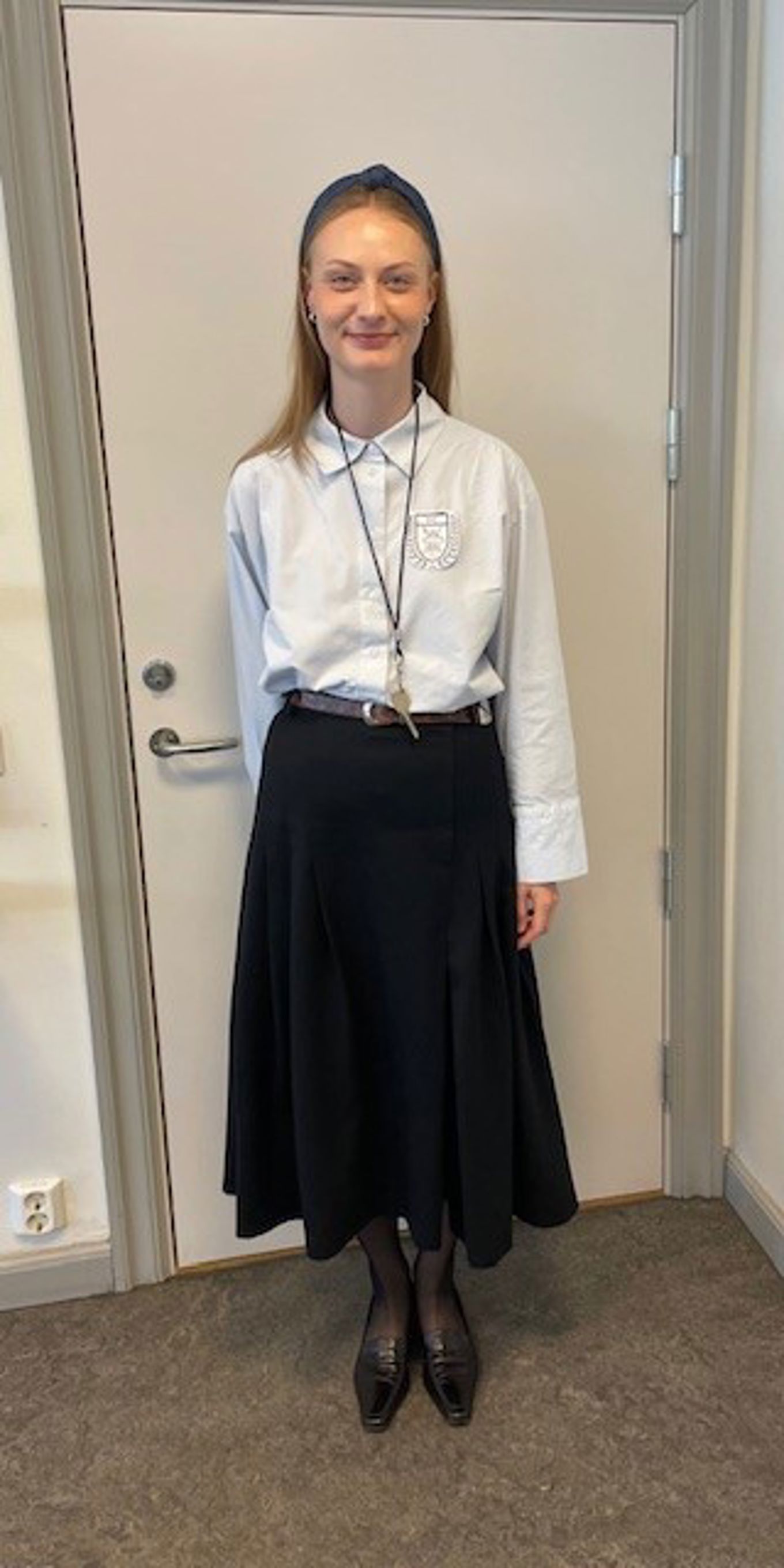 en lærer som har på seg skjørt og skjorte med skolens emblem